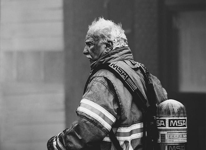 Schwarz-weiß-Bild eines Feuerwehrmanns in Schutzausrüstung mit einem MSA-Atemschutzgerät auf dem Rücken, von hinten zu sehen.