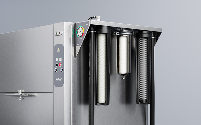 Close-up of stainless steel filtration system with three vertical cartridges and control panel with gauge