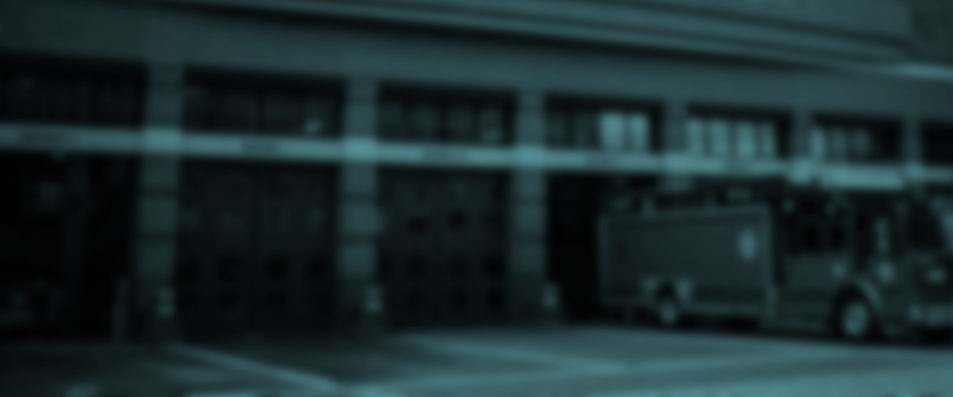 Blurred image of a fire station with garage doors and a fire truck on the righ.