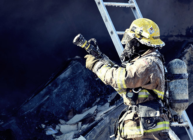 Ein Feuerwehrmann in voller Ausrüstung, hält einen Feuerwehrschlauch und trägt kontaminierte Ausrüstung.